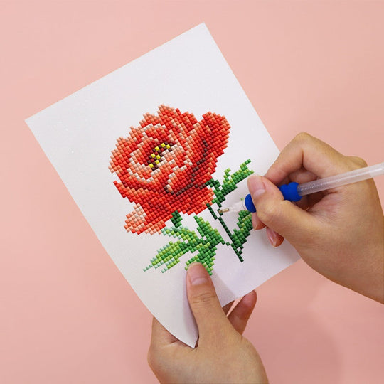 Diamond Painting Cross stitching a red rose on white fabric with a pink background